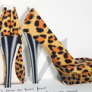 May include: A pop-up card featuring a high-heeled shoe with a leopard print design in shades of orange, brown, and black. The shoe has a black stiletto heel and a platform sole. The card is white with the text "It's time to have fun!"