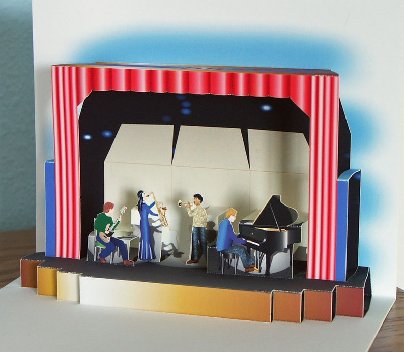 May include: A pop-up card depicting a jazz band on stage. The stage features a red curtain, a black backdrop, and a bandstand. Musicians play a guitar, saxophone, trumpet, and piano. The card is made of paper and has a three-dimensional effect.