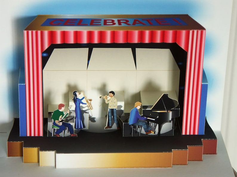 May include: A pop-up card featuring a stage with a band playing instruments. The stage has red curtains and the word "CELEBRATE!" across the top. The band includes a guitarist, a saxophonist, a trumpet player, and a pianist.