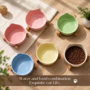 May include: Five round ceramic bowls with cat-ear shaped rims, each resting on a small wooden stand. The bowls are colored pink, light green, light blue, yellow, and white, with the white bowl filled with brown dry food. Text reads: Water and food combination Exquisite cat Life.