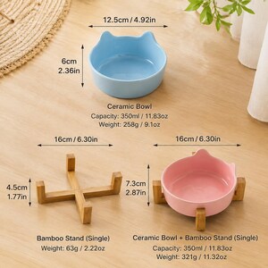 May include: A light blue ceramic bowl with cat-ear shaped rims, a pink ceramic bowl with cat-ear shaped rims, and a bamboo stand. The blue bowl is 4.92 inches wide and 2.36 inches high. The bamboo stand is 6.30 inches wide and 1.77 inches high.