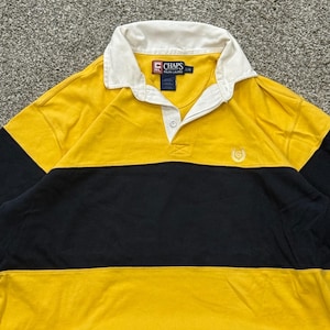 May include: A long-sleeve rugby shirt featuring a color-blocked design in yellow and navy blue. The shirt has a white collar, a button placket, and a small embroidered logo on the chest. The interior label reads Chaps Ralph Lauren size L/G.