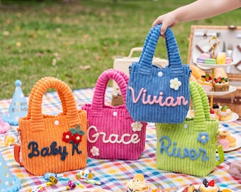 May include: Four small corduroy tote bags in orange, pink, blue, and lime green. Each bag features a white snap closure, two handles, and a personalised name embroidered in cursive: Baby K, Grace, Vivian, and River, with floral accents.