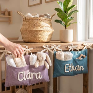 Peut inclure: Deux organisateurs suspendus en tissu avec des poches, l'un violet poussi&eacute;reux avec le nom Clara et l'autre bleu sarcelle avec le nom Ethan. Chaque organisateur pr&eacute;sente des lettres brod&eacute;es blanches et est attach&eacute; &agrave; une surface en bois.