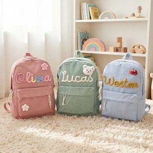 May include: Three corduroy backpacks in pink, sage green, and light blue. Each bag features a front pocket, white zipper pulls, and a personalized name in raised lettering. The pink bag has flower patches, the green has a bear, and the blue has a car.