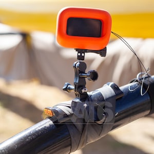 May include: A bright orange action camera housing mounted on a black pole using an adjustable black plastic bracket. The camera is secured with a black strap and features a small orange tab with the text SEATS visible on the mounting base.