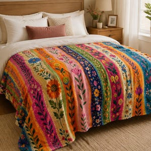 May include: A bed blanket featuring a vibrant vertical striped pattern with various floral motifs in shades of orange, pink, blue, and green. The design includes sunflowers and smaller wildflowers arranged in repeating columns across the fabric surface.