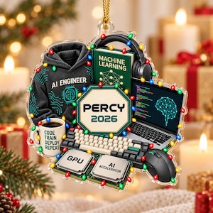 May include: A decorative ornament featuring a black hoodie with AI ENGINEER text, a green book titled MACHINE LEARNING, a laptop with code and a brain graphic, a keyboard, a mouse, two computer chips labeled GPU and AI ACCELERATOR, a mug with CODE TRAIN DEPLOY REPEAT text, and a central sign reading PERCY 2026, all surrounded by colorful Christmas lights.