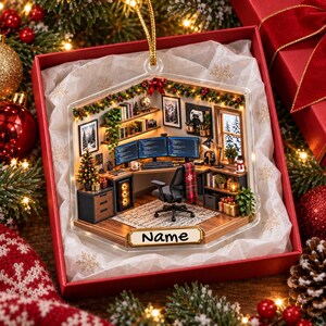 May include: A clear, hexagonal-shaped Christmas ornament featuring a miniature 3D office scene with a desk, three computer monitors displaying code, a chair, and shelves. The ornament includes a gold hanging string and a label with the text Name.