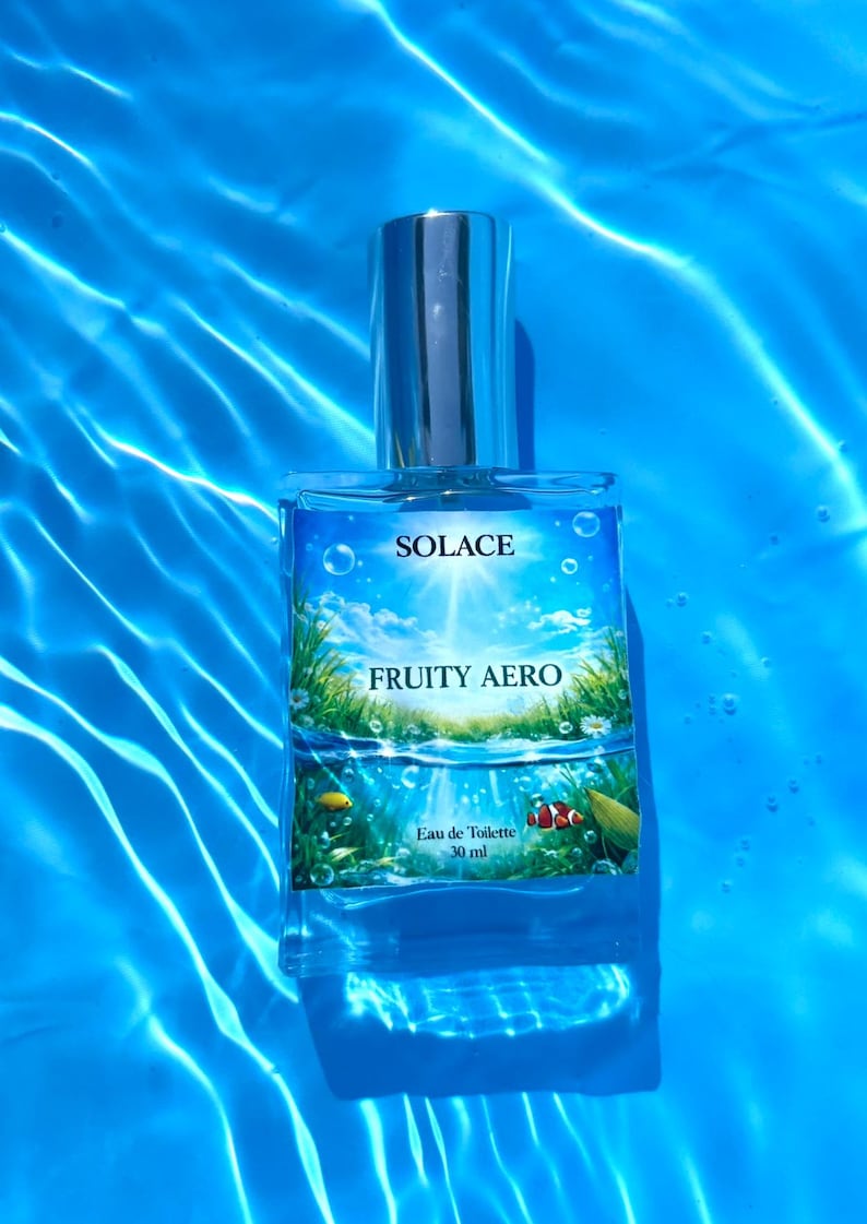 Puede incluir: Un frasco de perfume rectangular de cristal con tap&oacute;n plateado, etiquetado como Solace Fruity Aero Eau de Toilette 30 ml. La etiqueta muestra un cielo brillante, hierba verde e im&aacute;genes submarinas con peces sobre un fondo de agua azul.