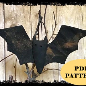 May include: A black fabric bat ornament with small black bead eyes and outstretched wings, suspended by a thin black string. A yellow oval graphic in the bottom right corner contains the black text PDF PATTERN in a bold serif font.
