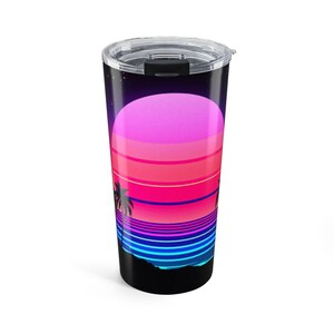 Op de afbeelding: Een cilindervormige roestvrijstalen beker met een doorzichtig plastic deksel en een grafische print van een zonsondergang boven de oceaan. Het ontwerp toont een grote roze en rode zon boven horizontale blauwe en paarse strepen met zwarte palmbomen.
