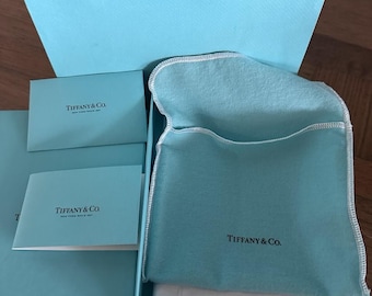 Set regalo Tiffany & Co. comprensivo di scatola, carta velina, sacchetto in feltro, libretto per la cura della pelle e borsa.