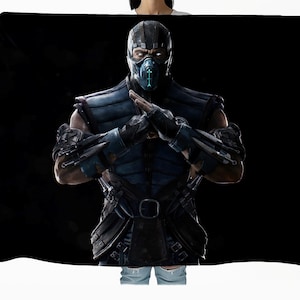 May include: A rectangular throw blanket featuring a high-resolution graphic of the Mortal Kombat character Sub-Zero. The character wears a dark blue and black armored ninja suit with a matching mask, posing with arms crossed against a black background.