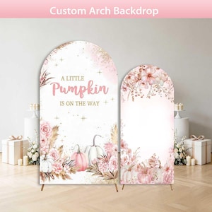 May include: Two arched fabric backdrops featuring a soft pink and white color palette with floral arrangements and pumpkins. The larger backdrop displays the text A LITTLE PUMPKIN IS ON THE WAY in gold lettering, accented by small gold star shapes.