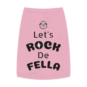 Puede incluir: Camiseta rosa claro para perros con el texto negro "Let's Rock De Fella", un dibujo de perro y las palabras "Stay Pawsitive". Ropa para mascotas.