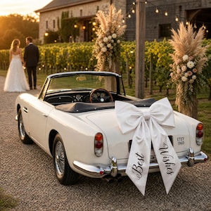 Peut inclure: Une voiture décapotable vintage blanche ornée d'un grand nœud en satin blanc sur le coffre. Le nœud porte l'inscription "Best Wishes" en écriture noire. La voiture possède des pare-chocs chromés, des roues à rayons et une plaque "ETSY 1960".