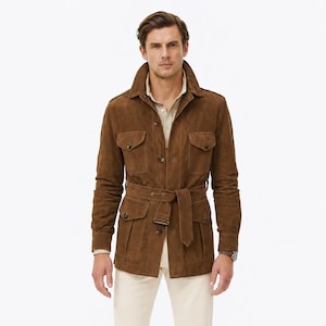 May include: A brown suede jacket with a belted waist, four front flap pockets, and a high collar, worn over a light beige button-down shirt and cream-coloured trousers, paired with dark brown suede shoes.