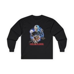 May include: A black long-sleeve shirt featuring a graphic print of the character Pinhead from Hellraiser. The design includes blue lightning, chains, and a puzzle box, with the red text HELLRAISER printed prominently below the central illustration.