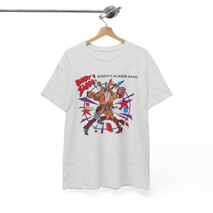 May include: A light gray short-sleeve t-shirt featuring a graphic print of two figures wrestling. The text "BODY SLAM!" appears in red, and "BOOTSY'S RUBBER BAND" is printed in black. The design includes colorful geometric shapes and star accents.