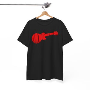 Pode incluir: Uma t-shirt preta de manga curta com um design gráfico vermelho em forma de guitarra elétrica. A palavra MONK está impressa em letras vermelhas grandes no corpo da guitarra e as letras BBS estão impressas ao longo do braço.