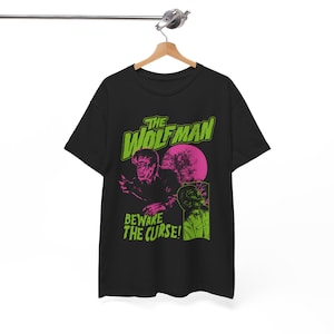 Könnte beinhalten: Ein schwarzes Kurzarm-T-Shirt mit einem Grafikdruck mit dem Text THE WOLFMAN und BEWARE THE CURSE! Das Design enthält eine grüne und rosa Illustration eines Werwolfs, einen großen rosa Mond und ein kleineres Einsatzfeld mit einer Person.