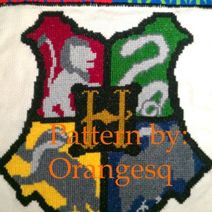 Puede incluir: Un patrón de punto de cruz blanco de los escudos de las casas de Hogwarts. Los escudos están en los colores de Gryffindor, Hufflepuff, Ravenclaw y Slytherin. El texto "Pattern by: Orangesq" está debajo de los escudos.