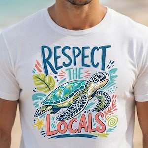 May include: A white t-shirt featuring a graphic illustration of a sea turtle swimming. The text "RESPECT THE LOCALS" is printed in blue and pink. The design includes colorful accents of a green leaf, a yellow starfish, and coral elements.