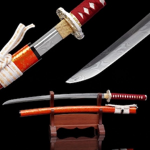 May include: A katana sword featuring a Damascus steel blade with a visible wavy pattern, a red cord-wrapped handle, and a gold-colored metal guard. The scabbard is bright orange with a glossy finish and is tied with a white braided cord.