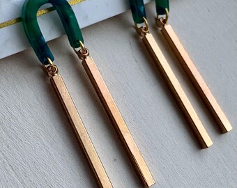 Peut inclure: Une paire de boucles d'oreilles pendantes rectangulaires dorées avec un dessus en forme d'arche vert et bleu. Les boucles d'oreilles sont suspendues sur une surface blanche. Design moderne et minimaliste.