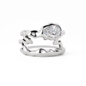 Peut inclure: Une bague argentée présentant un design de bande ouvert, fluide et organique avec une finition polie. La bague est ornée d'une unique pierre précieuse transparente à facettes en forme de poire, sertie dans la partie supérieure de la structure.