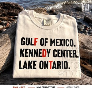 May include: A cream-colored t-shirt featuring black text that reads GULF OF MEXICO, KENNEDY CENTER, and LAKE ONTARIO. The letters F, D, and T are highlighted in red. The shirt has a crew neckline and a Comfort Colors brand label at the neck.