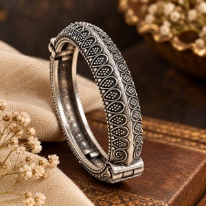 Può includere: Un bracciale rigido incernierato color argento con finitura ossidata e complessi motivi in rilievo a forma di goccia riempiti di piccoli punti. Il bracciale in metallo presenta un robusto meccanismo di chiusura e bordi testurizzati.