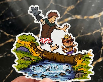 Puede incluir: Una pegatina troquelada con una ilustración de dibujos animados de una persona con chaleco marrón y pantalones cortos con corazones, caminando sobre un tronco sobre un arroyo junto a un gato con corona dorada y gafas de sol.