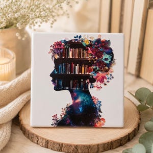 Op de afbeelding: Een vierkante witte keramische tegel met een silhouet van een menselijk hoofd in profiel. De binnenkant van het silhouet bevat boekenplanken en een kleurrijk sterrennevelpatroon, terwijl het haar is versierd met levendige bloemenillustraties.