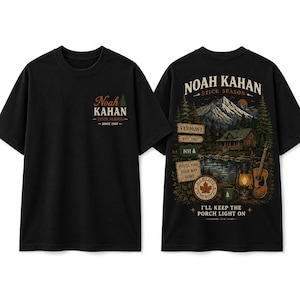 May include: A black short-sleeve t-shirt featuring a small Noah Kahan Stick Season logo on the front left chest. The back displays a detailed graphic of a mountain cabin, a lake, a guitar, a lantern, and text including Noah Kahan Stick Season.