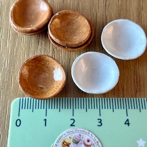 May include: Miniature wooden bowls in shades of brown and white. The bowls are arranged on a wooden surface next to a ruler. The ruler shows measurements in centimetres. The bowls are handmade.