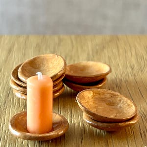 May include: A set of miniature wooden bowls and an orange candle. The candle is cylindrical and rests on a matching wooden dish. Several stacks of small, round wooden bowls are also visible, suggesting a decorative or functional set.