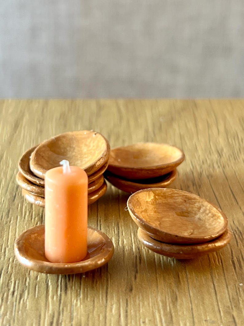 May include: A set of miniature wooden bowls and an orange candle. The candle is cylindrical and rests on a matching wooden dish. Several stacks of small, round wooden bowls are also visible, suggesting a decorative or functional set.