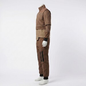 May include: A brown two-piece outfit consisting of a short-sleeved top and matching trousers. The top features a high collar, quilted paneling, and a geometric white line pattern on the sleeve. The trousers have black vertical accents on the legs.
