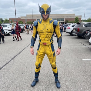 Peut inclure: Un costume complet de Wolverine composé d'une combinaison jaune et bleue avec des détails musculaires moulés, des épaulettes et des genouillères. La tenue comprend un masque assorti jaune et bleu à oreilles pointues et une boucle de ceinture rouge en X.