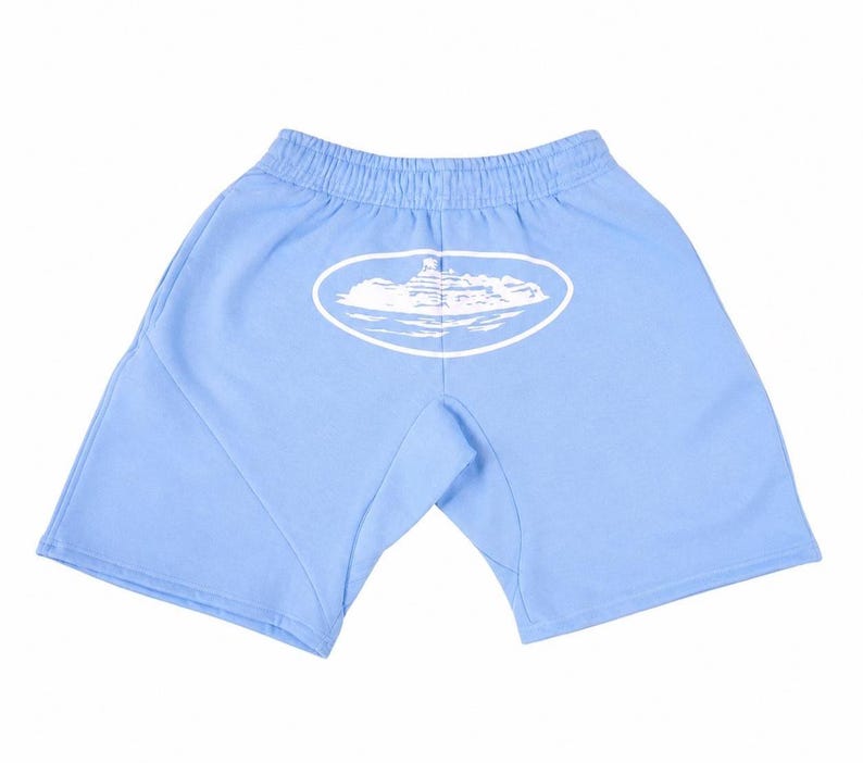 May include: Light blue shorts with an elastic waistband. A white oval graphic with a mountain and cloud design is printed on the back. The shorts are made of a soft material.