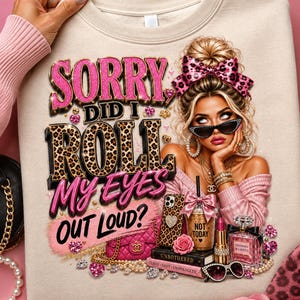 Peut inclure: Un sweat-shirt beige avec une illustration d'une personne aux cheveux blonds en chignon, portant un nœud léopard, des lunettes de soleil et des vêtements roses. Le texte SORRY DID I ROLL MY EYES OUT LOUD? est entouré d'accessoires comme un sac.