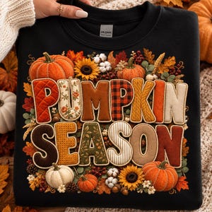 Op de afbeelding: Een zwart sweatshirt met ronde hals en een grafische print met de tekst PUMPKIN SEASON. De letters zijn gevuld met diverse herfstachtige patronen en texturen, omringd door illustraties van pompoenen, zonnebloemen, katoen en herfstbladeren.