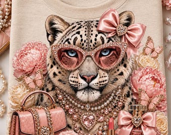 May include: A beige sweatshirt featuring a graphic of a leopard wearing pink rhinestone-encrusted cat-eye glasses, a pink satin bow, and layered pearl necklaces. The design includes pink roses, butterflies, a pink handbag, and perfume.