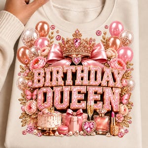 May include: A beige sweatshirt featuring a graphic print of the text BIRTHDAY QUEEN in pink glittery letters. The design includes a gold crown, pink balloons, flowers, a cake, a gift box, a perfume bottle, a lipstick, and a champagne glass.