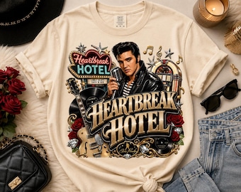 Könnte beinhalten: Ein beiges T-Shirt mit einem Grafikdruck von Elvis Presley, der ein Mikrofon hält, sowie einer Gitarre, einer Jukebox und einem Neonschild mit der Aufschrift Heartbreak Hotel. Das Design enthält Noten, Sterne, rote Rosen und den goldenen Text.