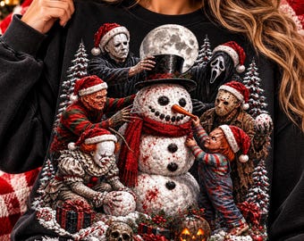 May include: A black sweatshirt featuring a graphic print of iconic horror movie characters wearing Santa hats and building a snowman. The scene includes a full moon, snow-covered pine trees, wrapped gifts, a skull, and a glowing jack-o'-lantern.