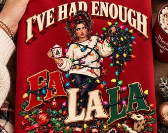 May include: A red sweatshirt featuring a graphic of a person wrapped in multicoloured Christmas lights, holding a mug with a tree print. The text reads I'VE HAD ENOUGH FA LA LA in bold, dimensional lettering, surrounded by ornaments and greenery.