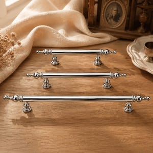May include: Three polished chrome cabinet pulls arranged in a vertical row, each featuring a long cylindrical bar, decorative finials at both ends, and two sturdy mounting posts with a rounded base design for secure attachment to furniture.
